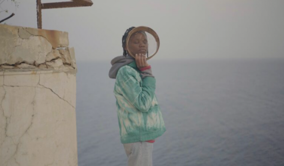 Image couleur, une jeune femme de couleur, les yeux fermés, debout devant la mer.